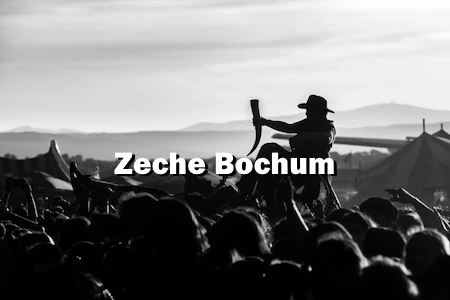 Hoch über den Köpfen, wird ein Mann im Rollstuhl getragen. Davor sieht man die Aufschrift Zeche Bochum