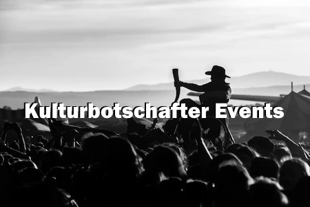 Hoch über den Köpfen, wird ein Mann im Rollstuhl getragen. Davor sieht man die Aufschrift Kulturbotschafter Events