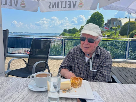 Herr G am Tisch mit Kaffee und Kuchen. Er trägt eine weiße Mütze und Sonnenbrille. Für ihn war die Kieler Woche ein tolles Erlebnis.