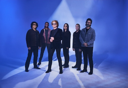 Die Band Simply red steht vor einem blauen Hindergrund. Insgesamt stehen 5 Mitglieder der Band hinder dem Sännger. Alle dunkel gekleidet