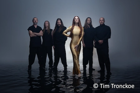 Die sechsköpfige Band Epica stehen im flachen Wasser. Die Sängerin tträgt ein goldenes Kleid. Die männlichen Musiker sind ganz in schwarz gekleidet.